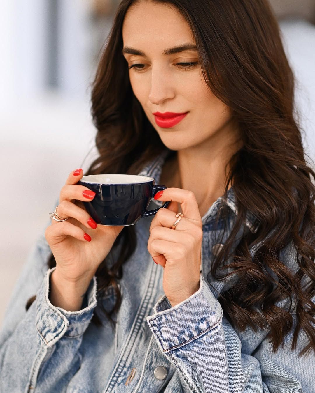 Close up of a woman holding a dark blue coffee mug with red manicured hands. Lifestyle business portrait in Valencia