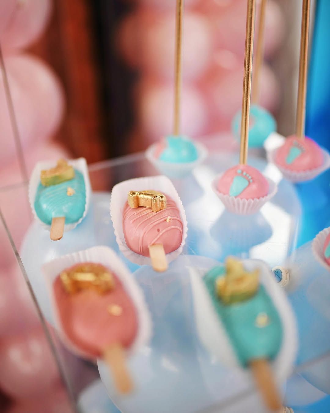 Detailed shot of pink and blue cakesicles with gold accents on a candy bar at an indoor gender reveal event in Valencia.