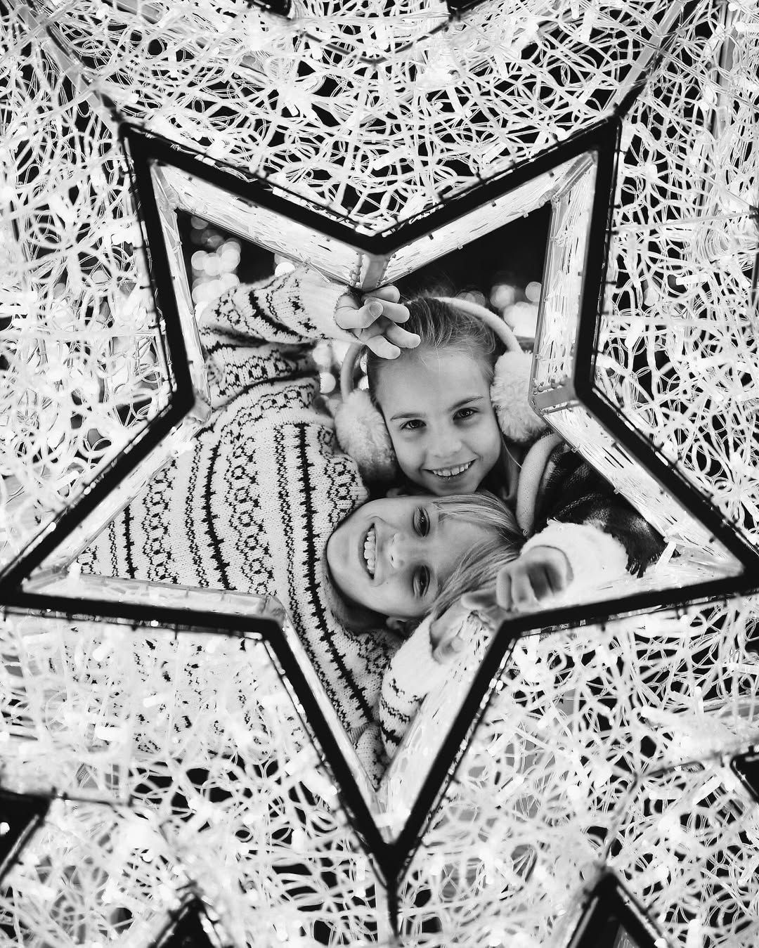 Black and white portrait of two smiling children looking through a large glowing star decoration in Valencia at Christmas.