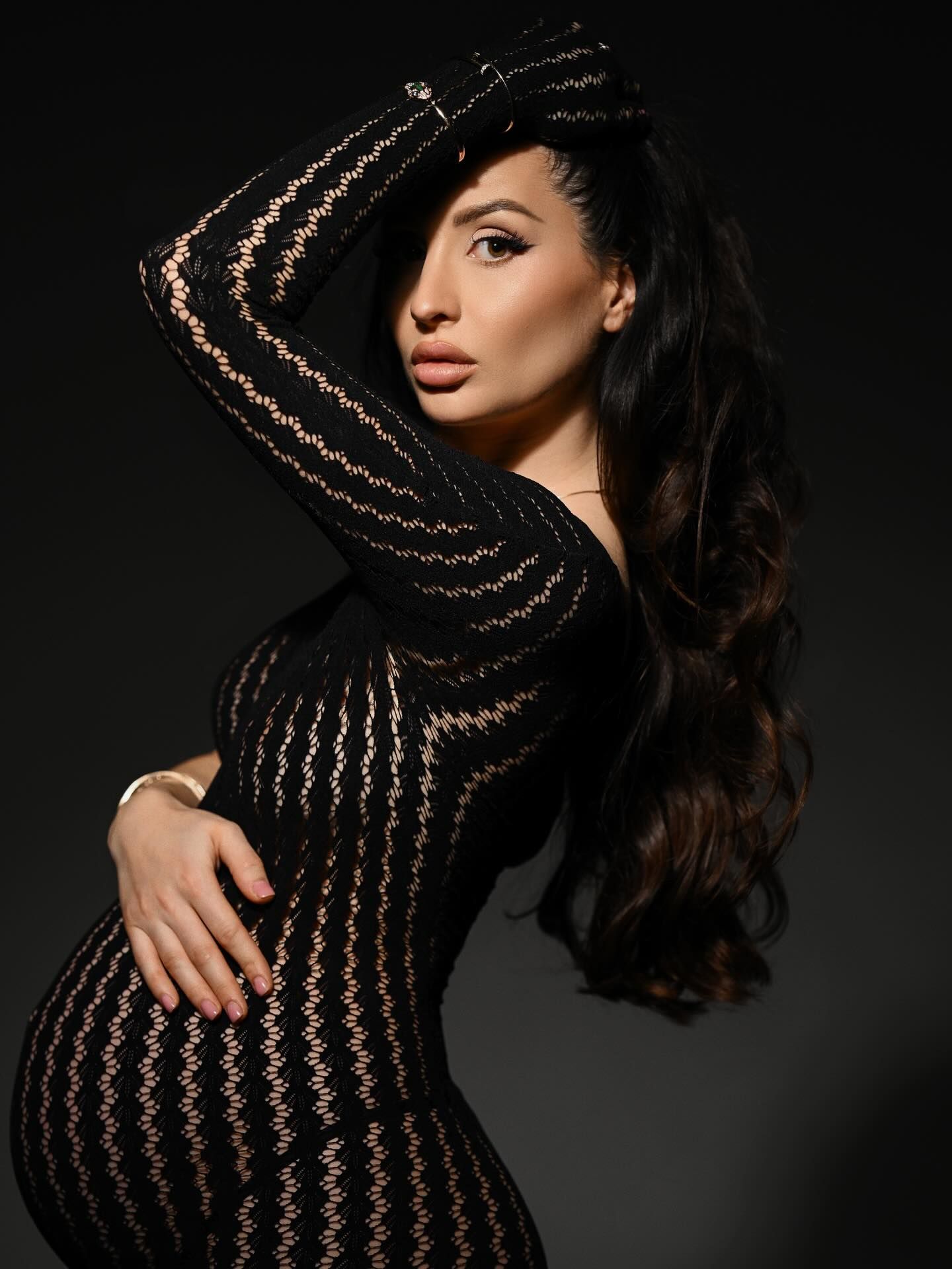 Artistic silhouette of a pregnant woman wrapped in mesh fabric against a dark background.
