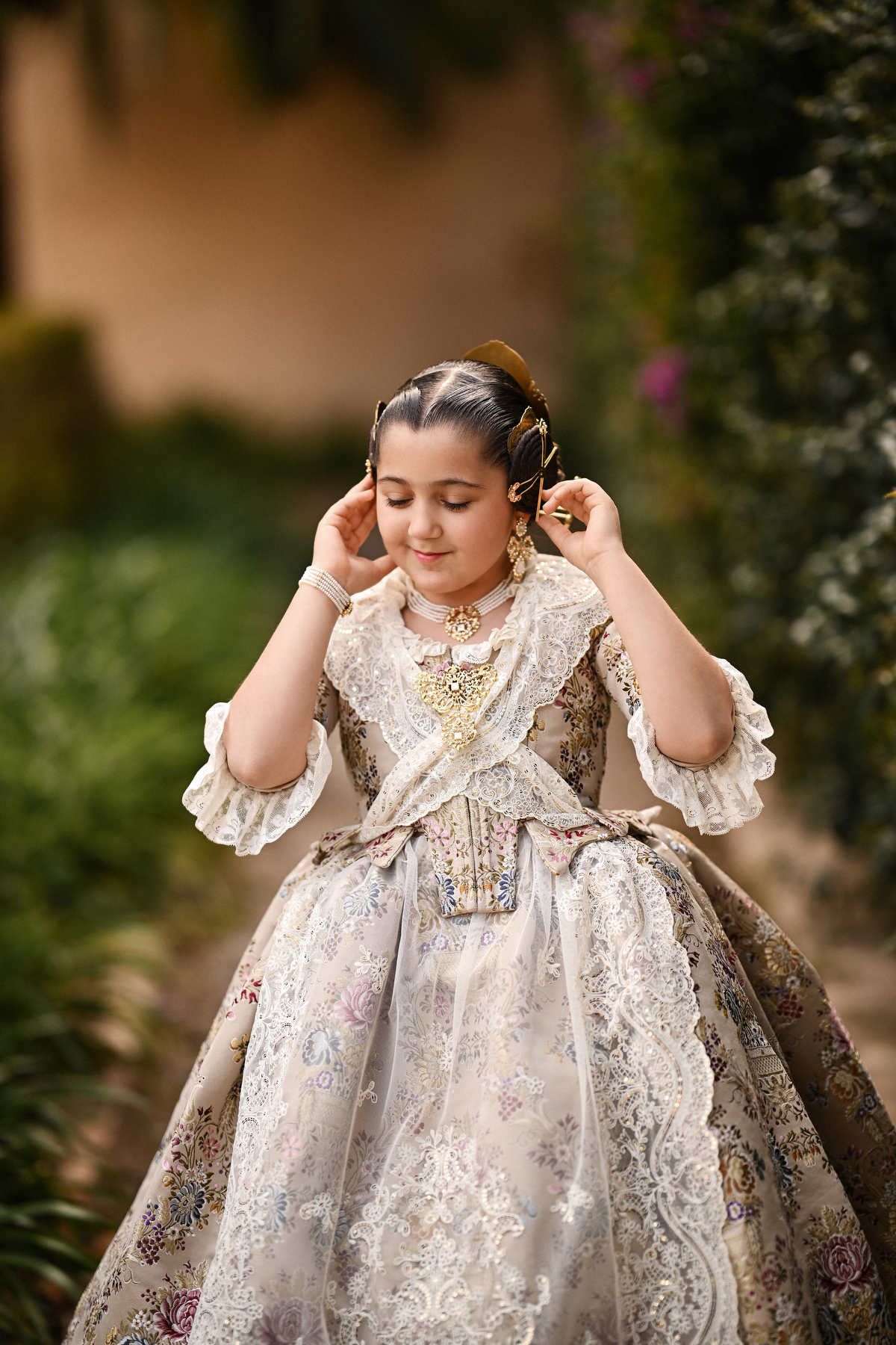A candid portrait of a young girl in traditional Fallera attire, gently adjusting her ornate golden peineta hair comb in the gardens.
