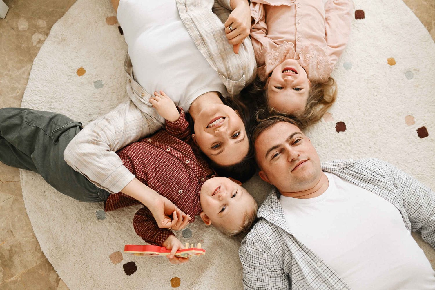 An overhead shot of a happy family lying together in a circle on a rug, smiling up at the camera during a candid home photo session.
