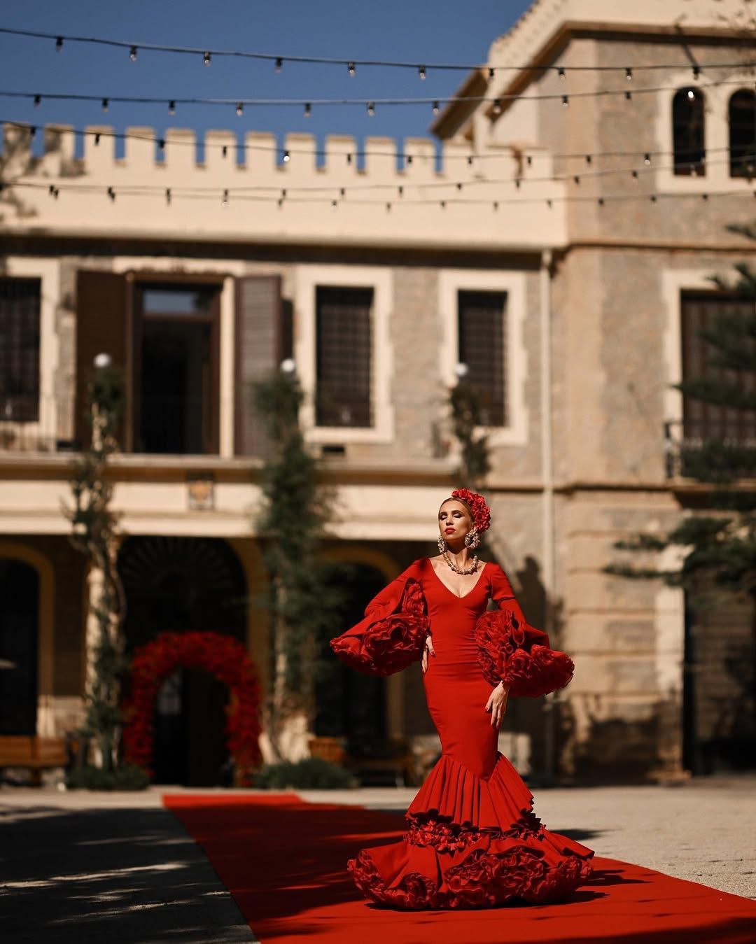 Full-length shot of a woman in a red dress walking the red carpet against the scenic architecture facade of Villa Montemolar