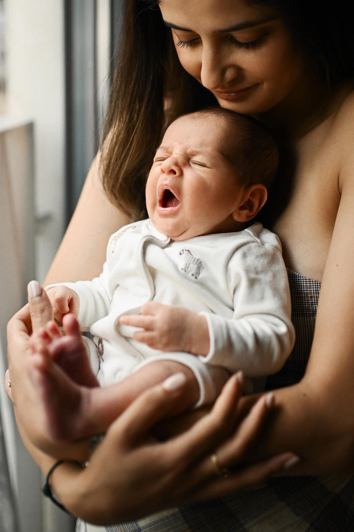 A mother holding her yawning newborn baby close during an authentic lifestyle photo session.