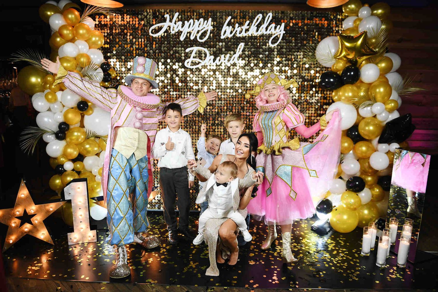 A lively group photo of children, family members, and bright costume animators posing together at a themed birthday photo zone.