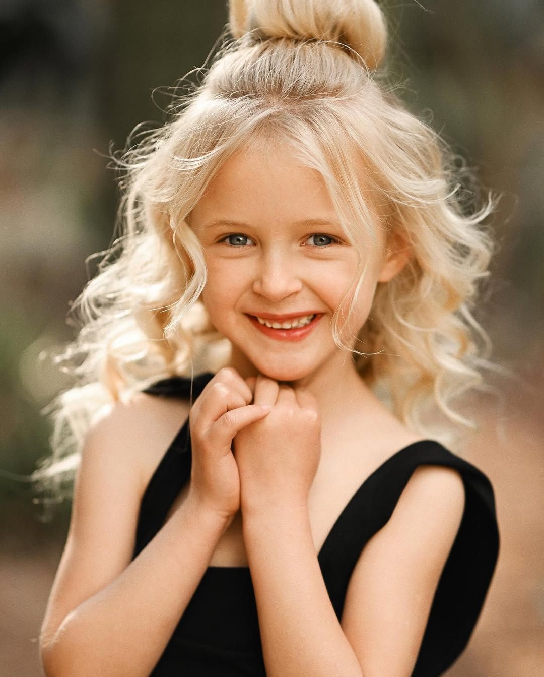 A close-up portrait of a blonde girl with curly hair smiling during a session at the Botanical Garden in Valencia.