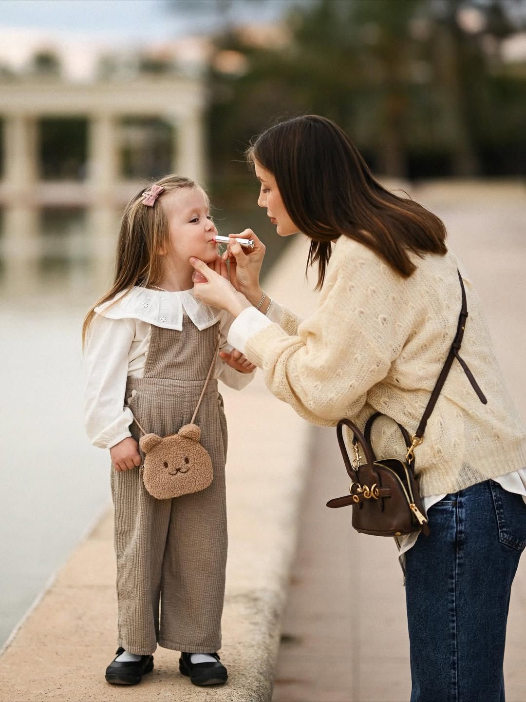 Mother helping her daughter with lip balm before a maternity session in Turia Park, Valencia beside the peaceful park waterways.