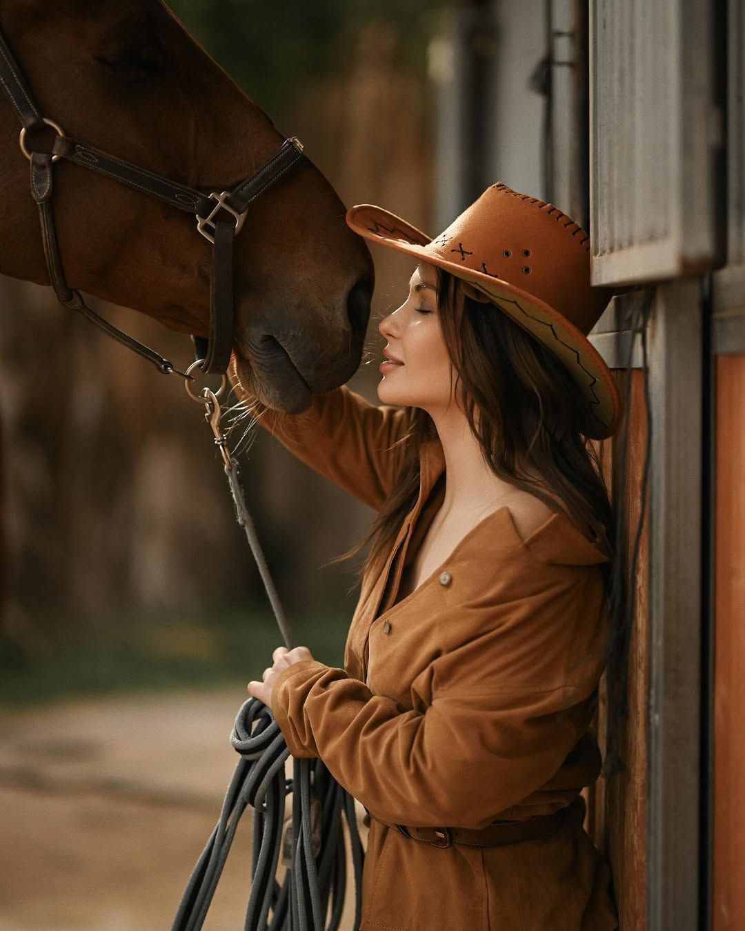 A cinematic close-up of a woman in a cowboy hat gently touching a horse at a stable during a premium photoshoot with make-up and stylist