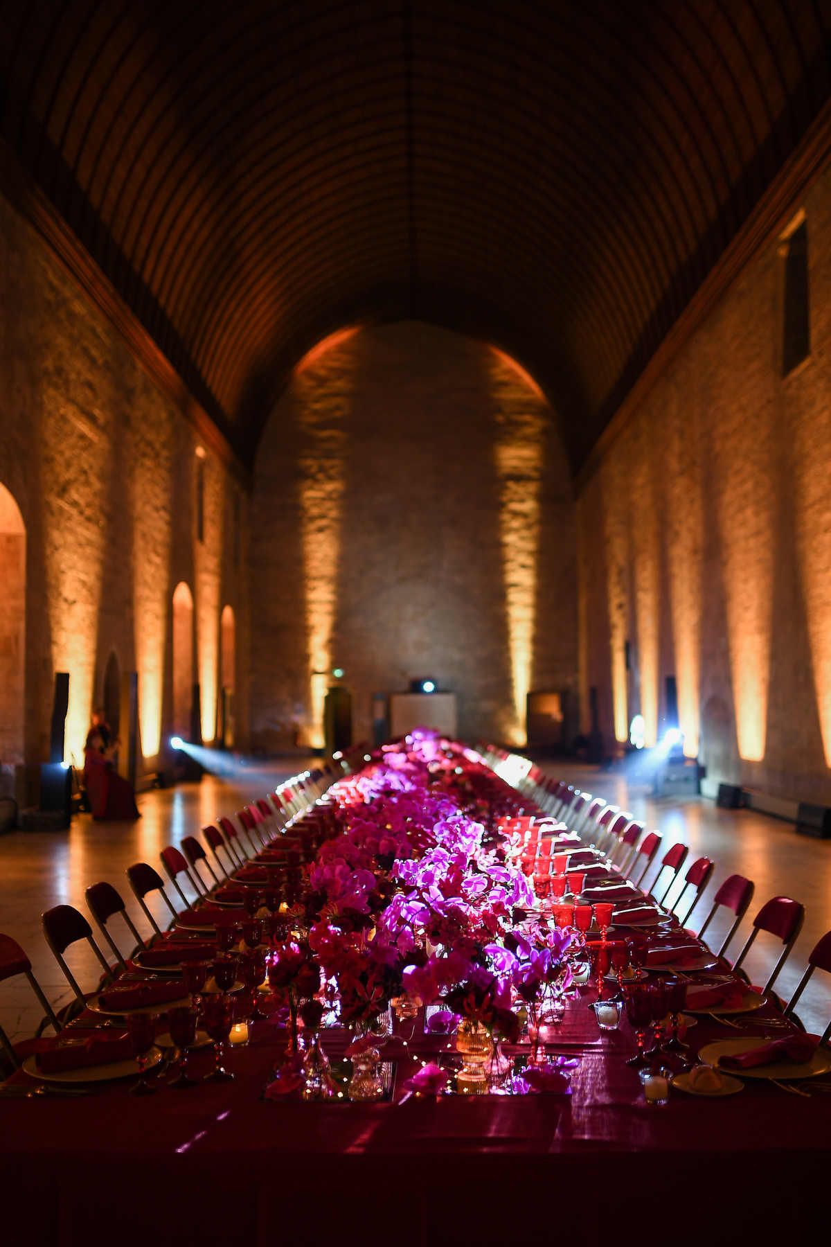 Grand event hall with a long dining table decorated with purple orchids and dramatic ambient spotlighting.