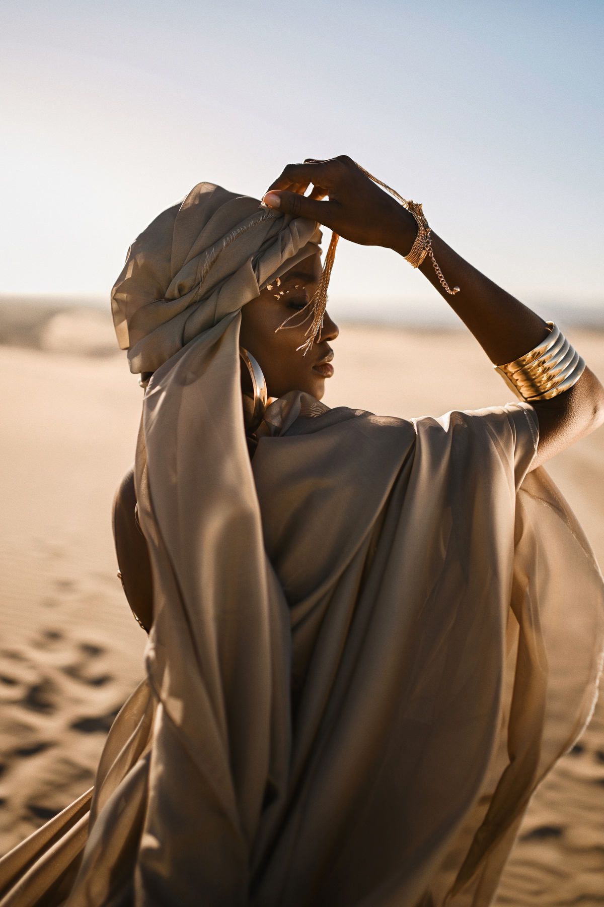 A model posing gracefully on sand dunes in a flowing editorial gown for a high-end commercial fashion production.
