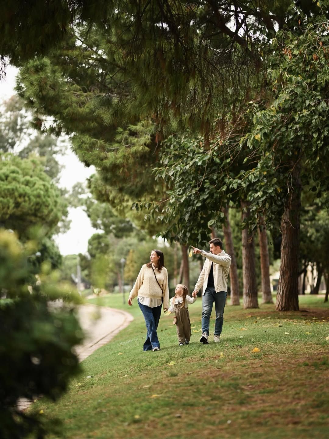 Expecting couple with their daughter during a maternity session in Turia Park, Valencia, surrounded by soft greenery and gentle shade.