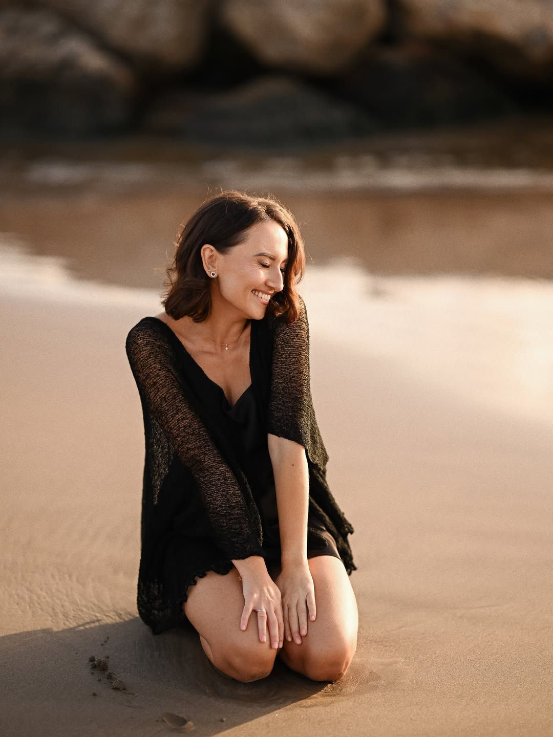 Candid women's portrait on a Valencia beach, showing a joyful woman kneeling on the sand and smiling under soft evening light.