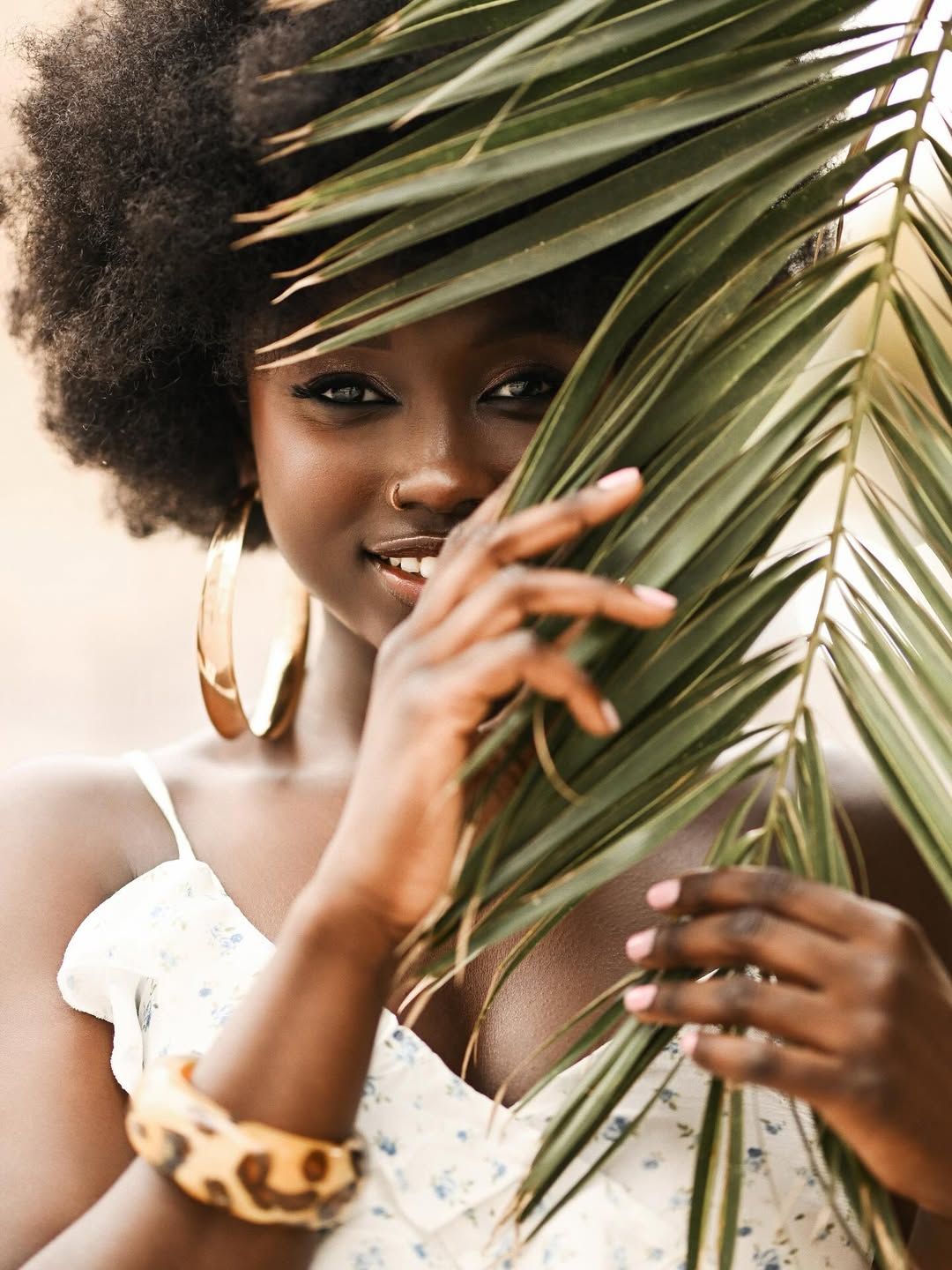 Close-up portrait of a smiling woman partially covering her face with a palm branch during a creative photoshoot in Alicante.