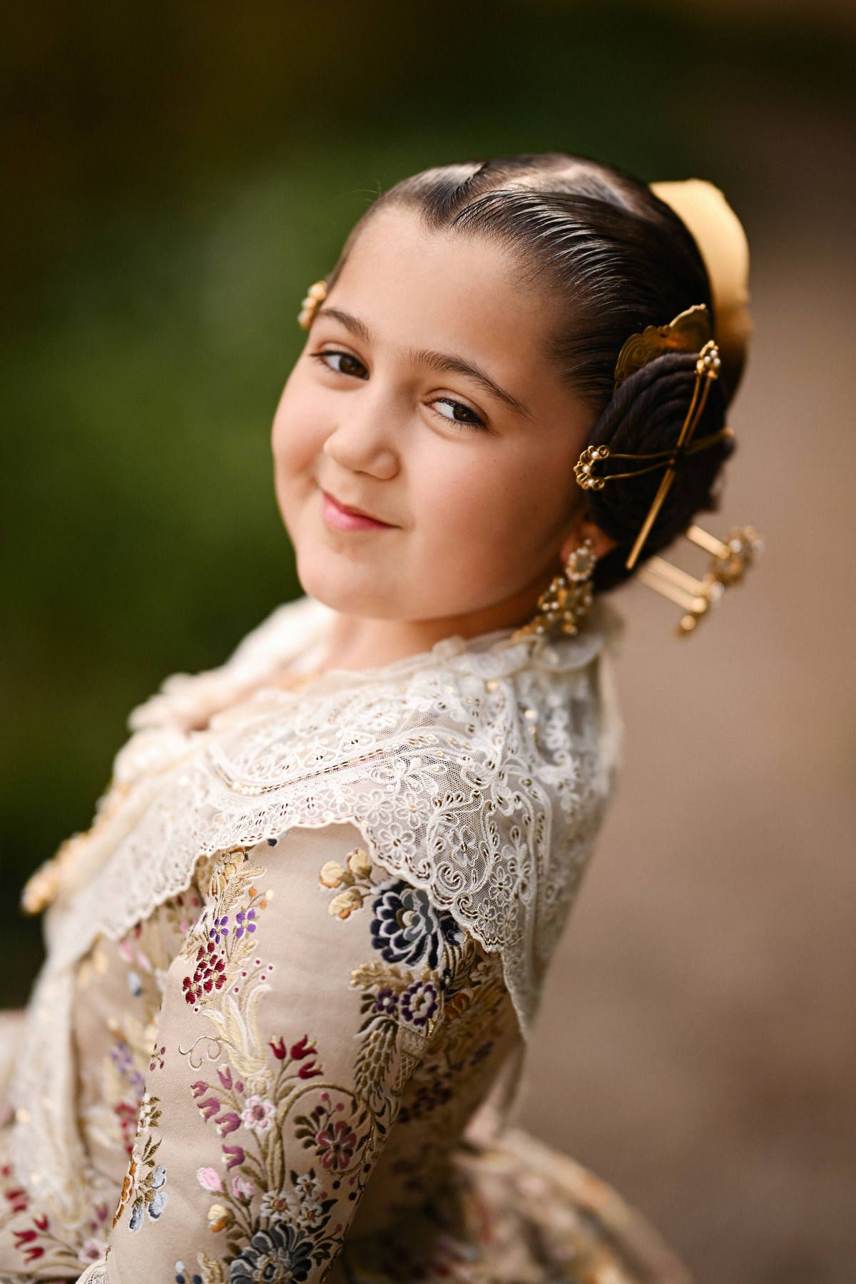 A soft close-up portrait focusing on the detailed Fallera hairstyle, pearl aderezos, and the delicate lace manteleta worn by a young girl.