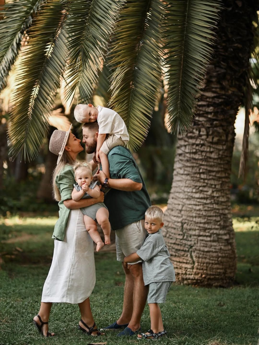 A family playing in Turia Park with the father holding his baby while the mother and son embrace nearby.