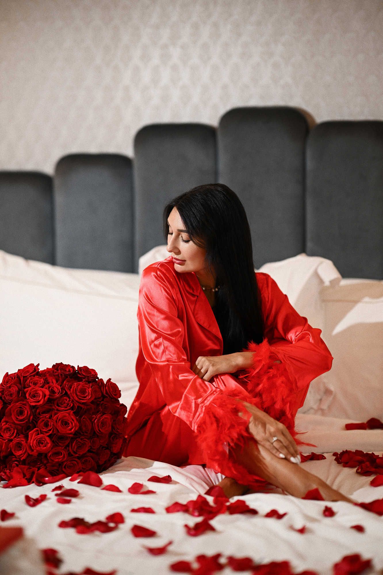 Second look of the Valencia bachelorette session featuring the bride in red feathered pyjamas sitting near a rose bouquet.