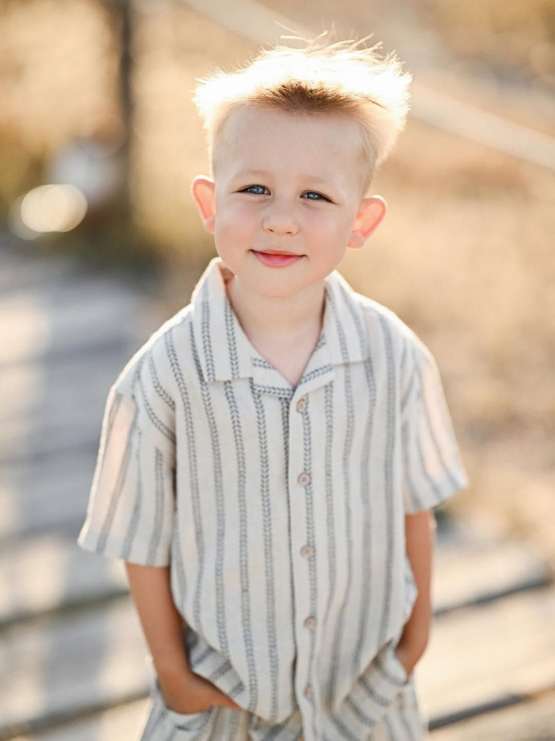 Soft backlit portrait of a young boy standing with hands in his pockets on a boardwalk in El Saler, Valencia.