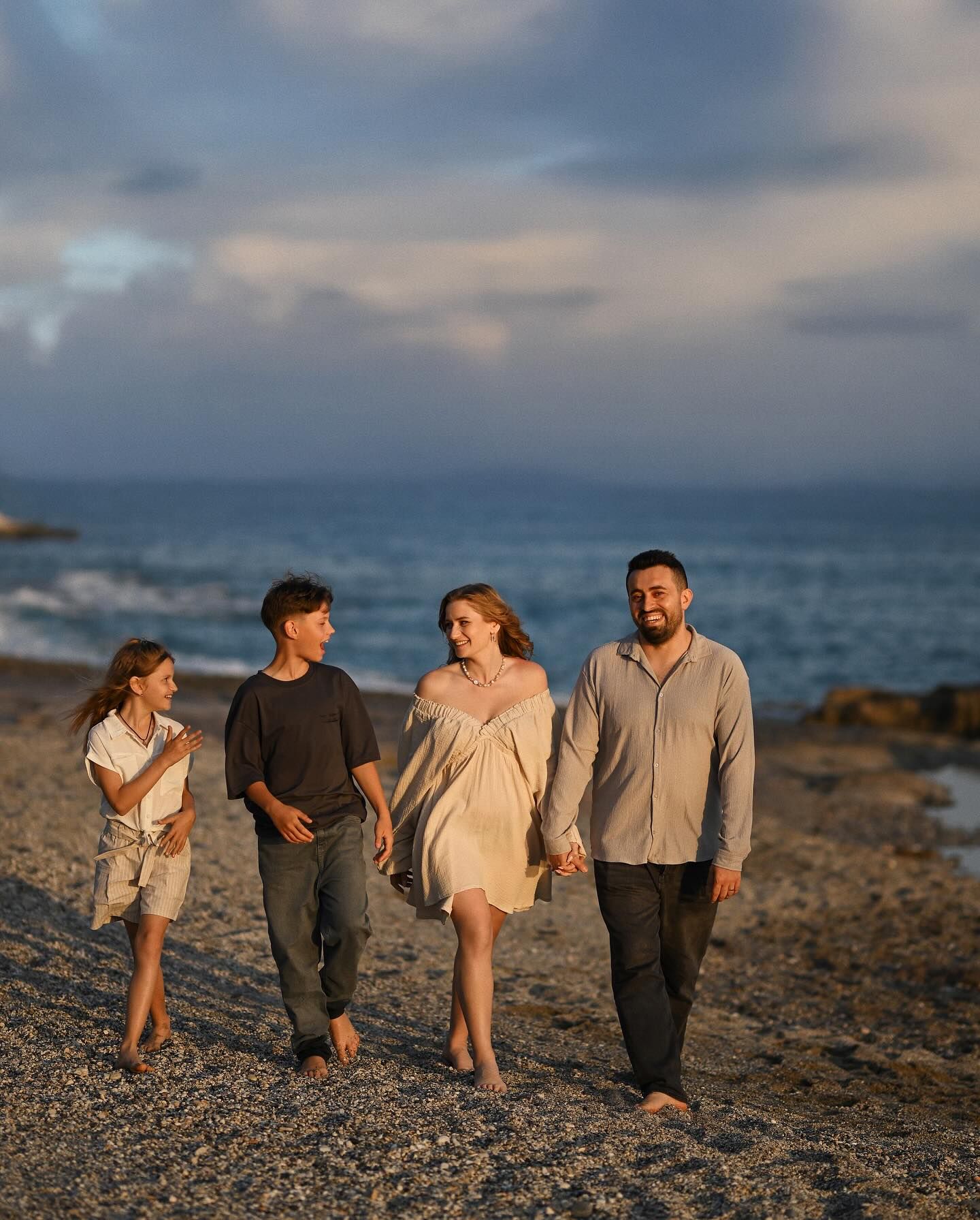 Full-length portrait of a family with two children walking along a pebble beach at sunset in Costa Blanca.