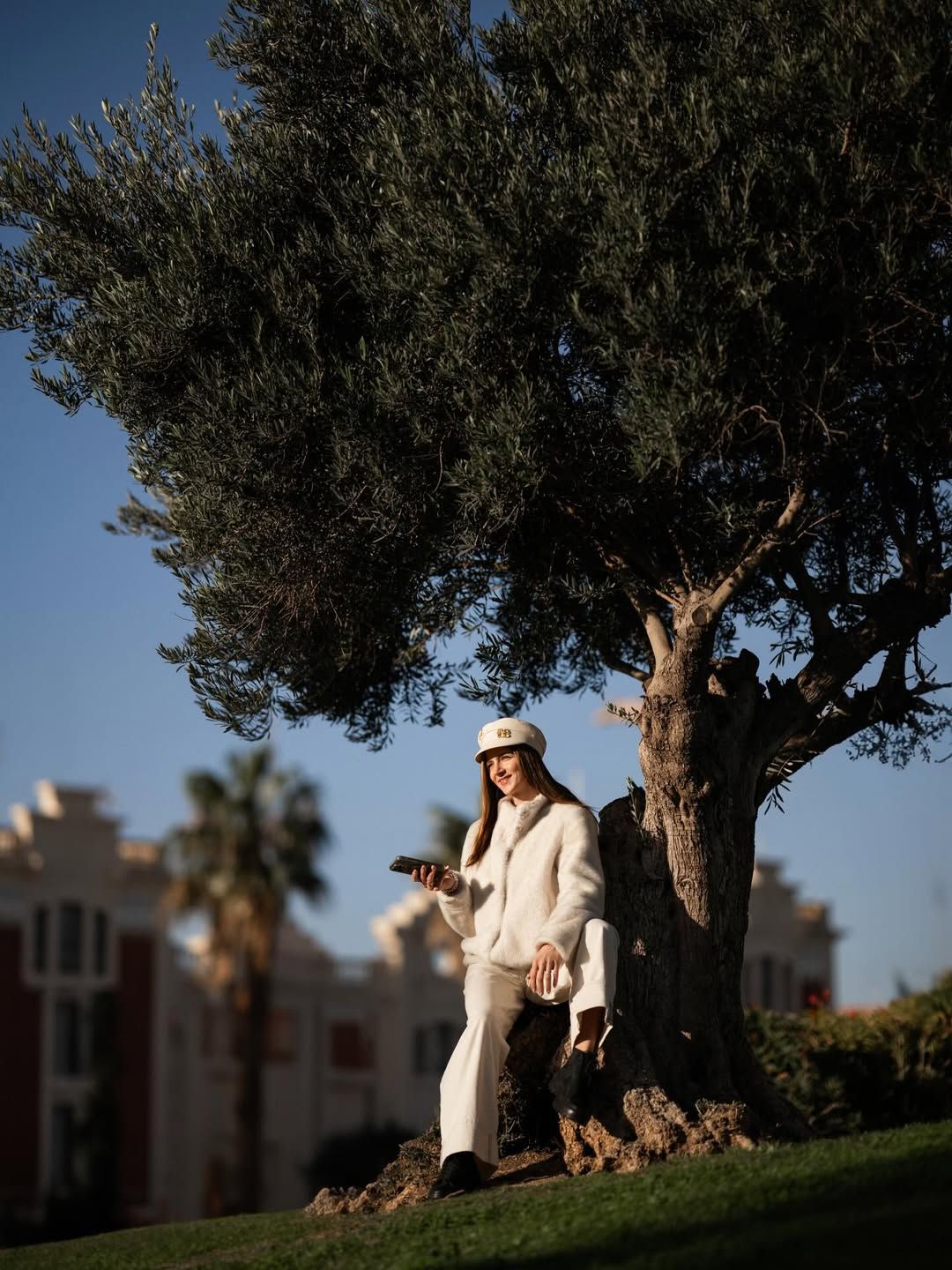 Woman in white leaning against a large olive tree at the Marina in Valencia during a portrait session