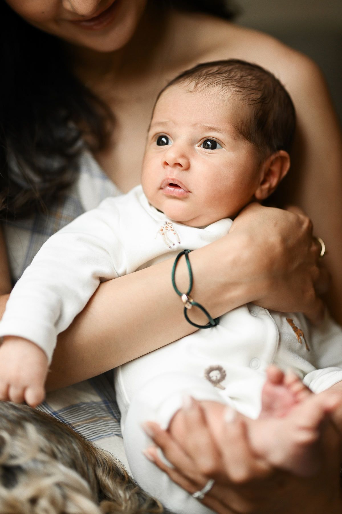 Lifestyle newborn and baby photography in Valencia showing a close-up portrait of a baby looking up while being held in mother's arms.