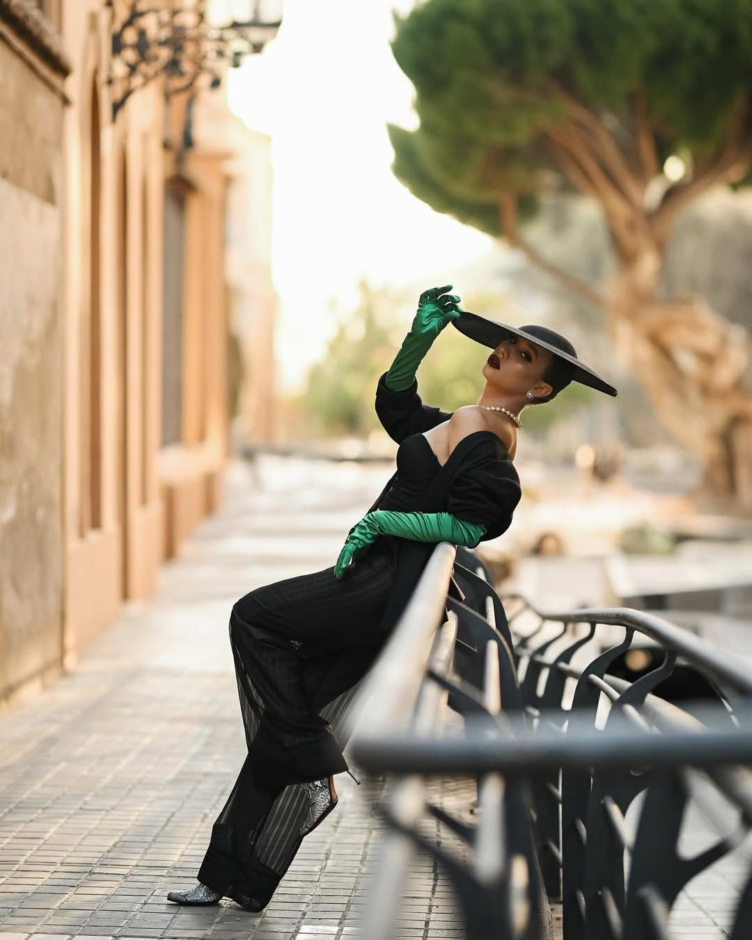 A woman with expert styling and makeup leaning on a city railing, capturing a sophisticated fashion mood in Valencia.