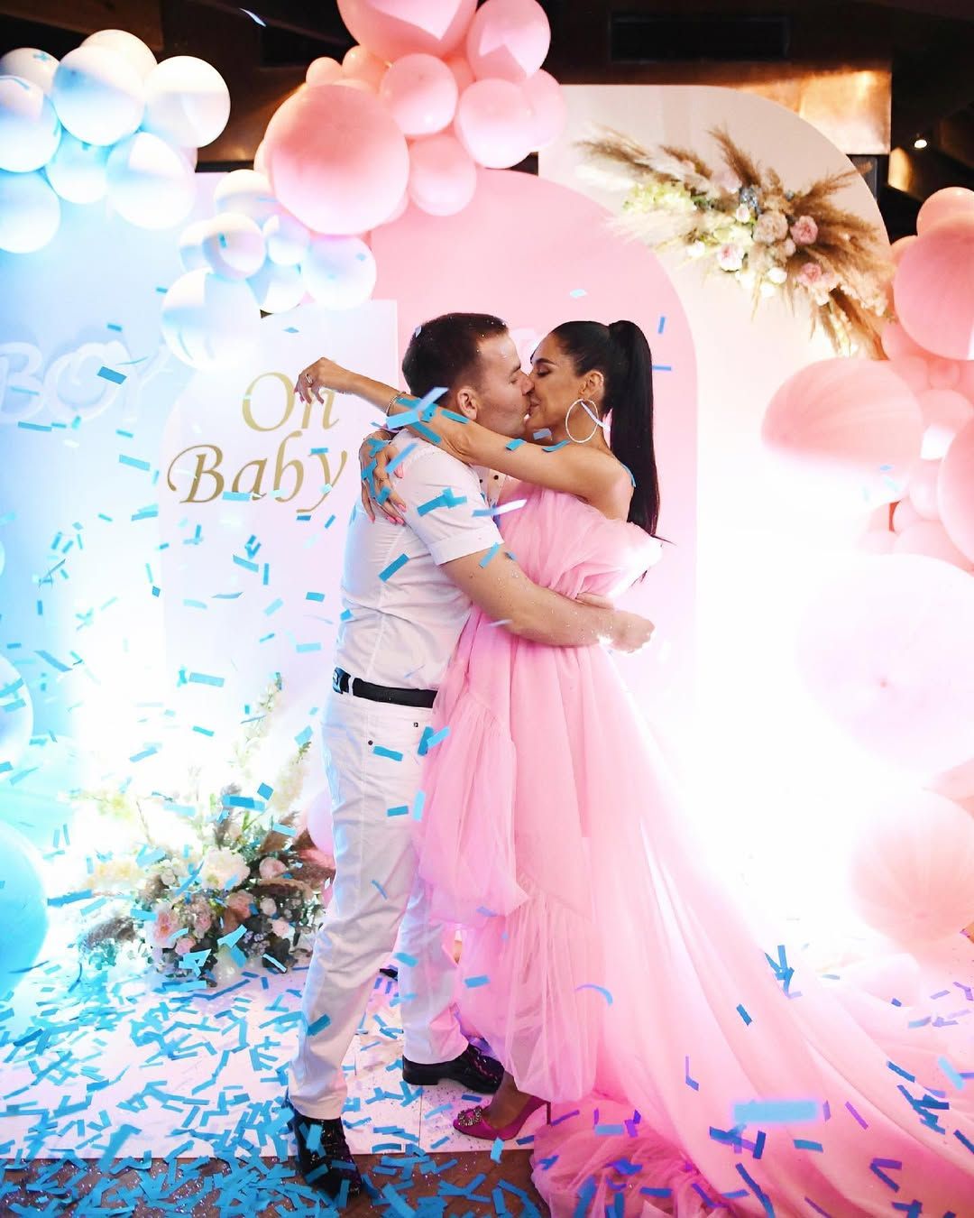Expecting couple kissing as blue confetti falls, revealing they are having a boy at their indoor gender reveal party in Valencia.