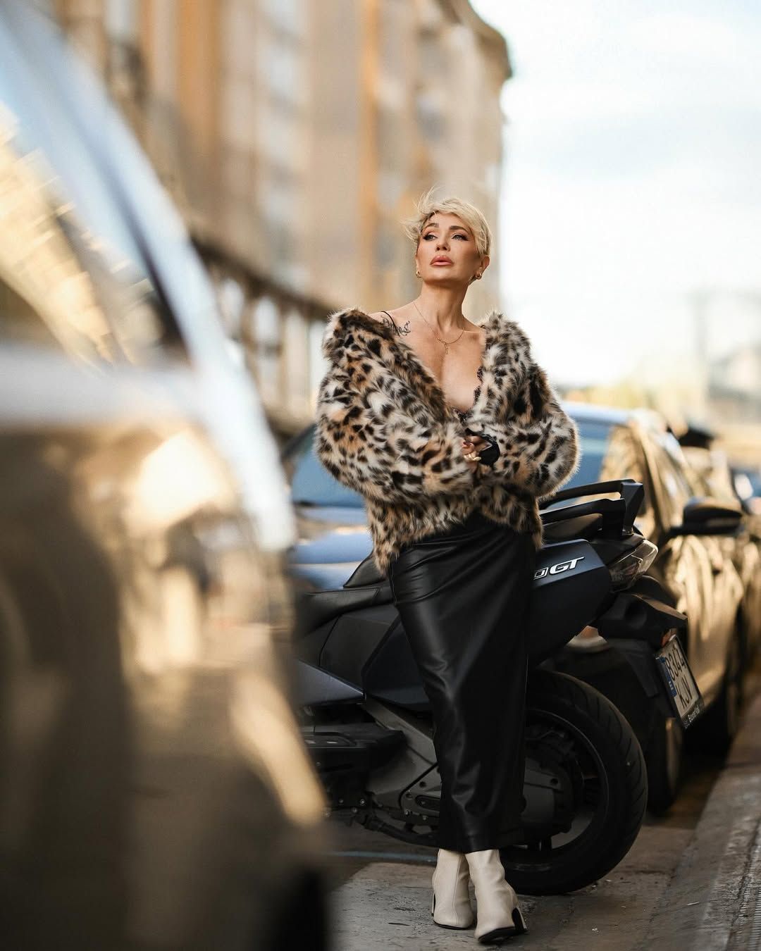 A high-end styled woman posing elegantly next to a motorcycle on a city street, capturing a premium editorial aesthetic.