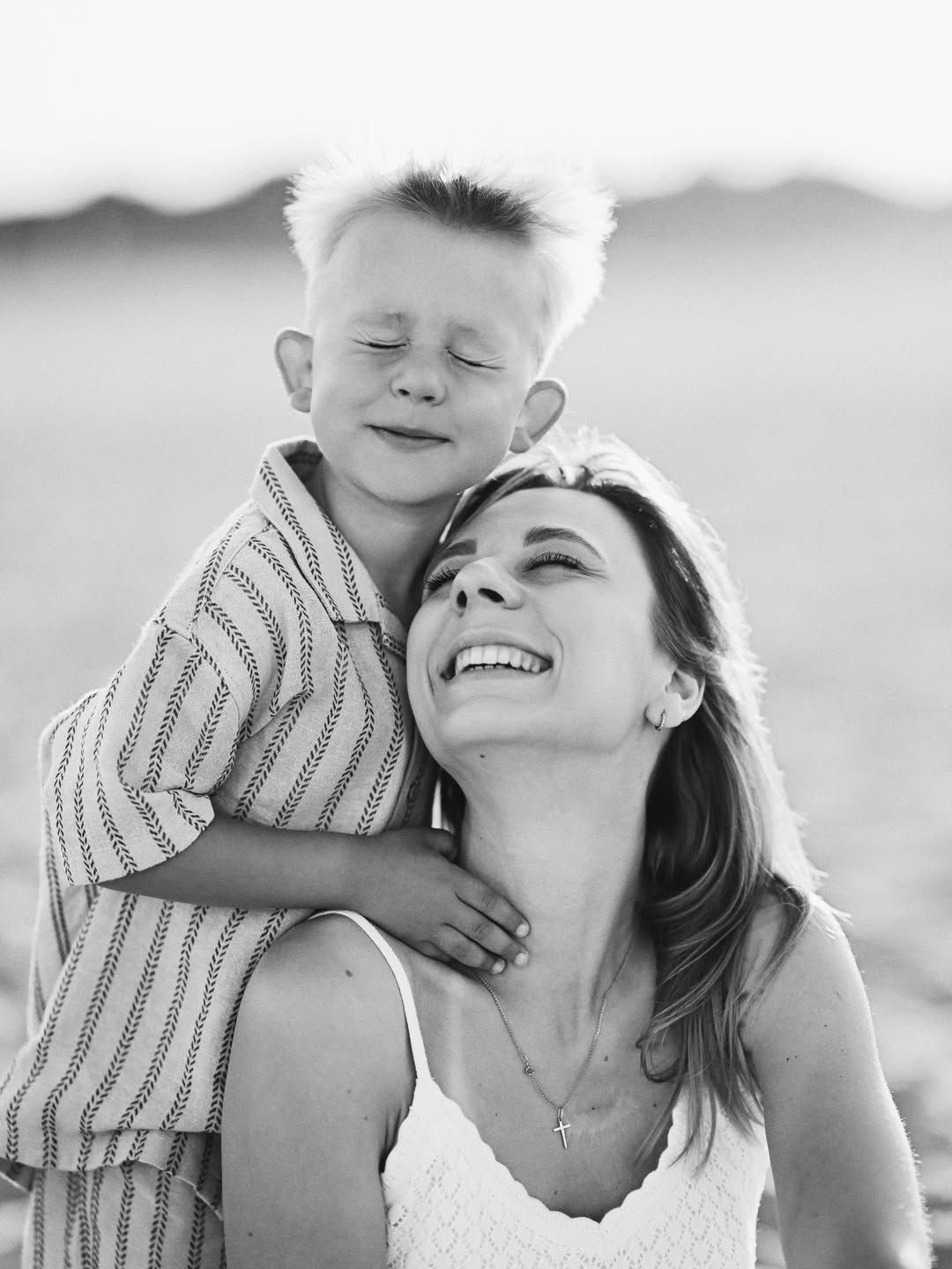 Black and white mother and son photoshoot capturing a joyful hug on the sandy shores of El Saler in Valencia.