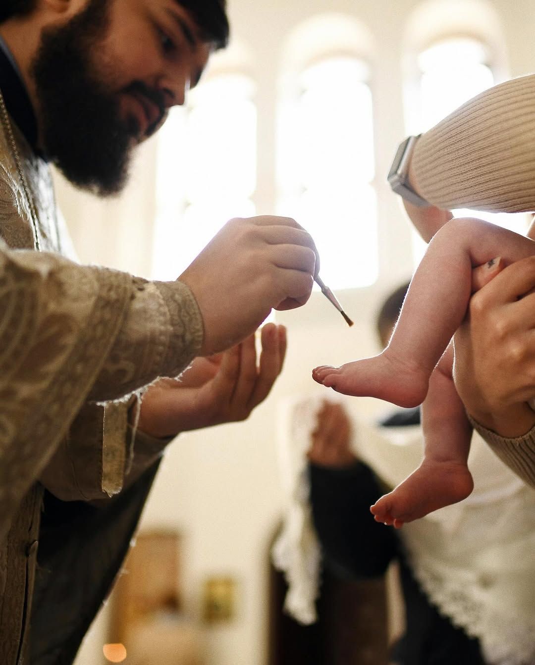 Close-up of a priest anointing a baby's feet with holy oil during a sacred christening ritual in a Valencia church.