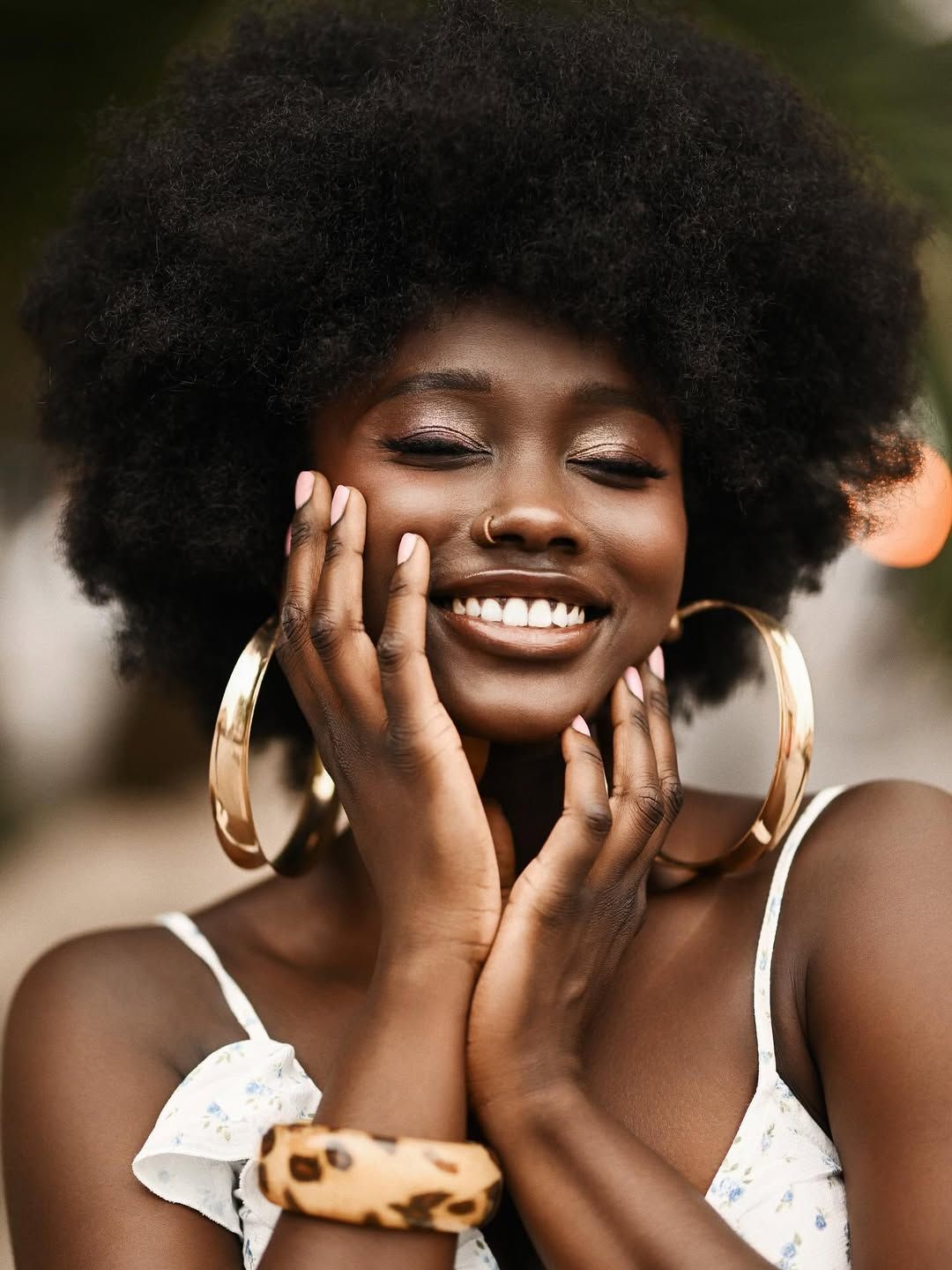 Close-up beauty portrait of a smiling woman with closed eyes holding her face, showcasing gold hoop earrings in Alicante.