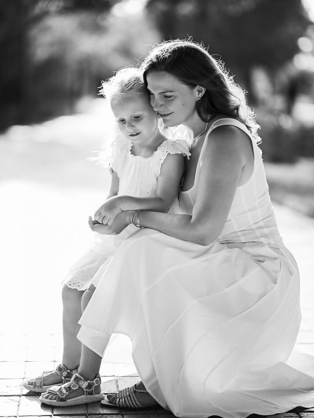 A black and white shot of a mother kneeling to hug her daughter on a forest path in the El Saler natural park.