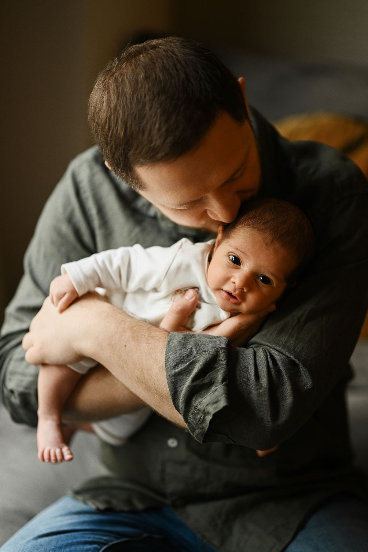 Father cradling his newborn baby securely in his arms during a lifestyle family photography session.