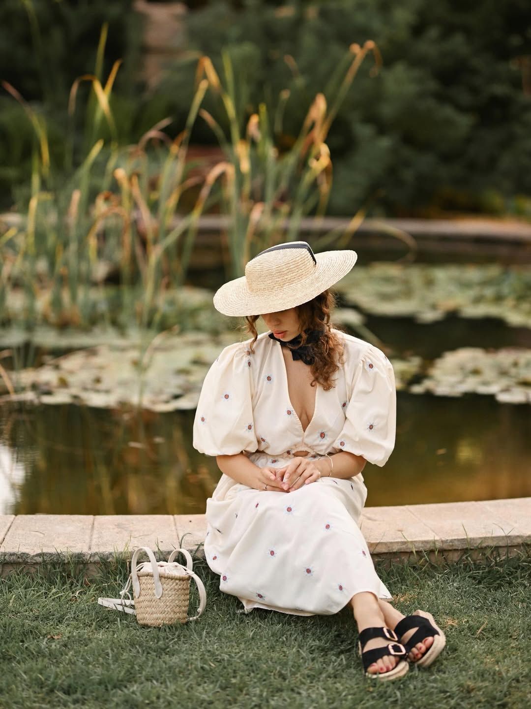 A thoughtful women's portrait of a lady sitting by a peaceful lily pond on a stone ledge during an outdoor session in Valencia.