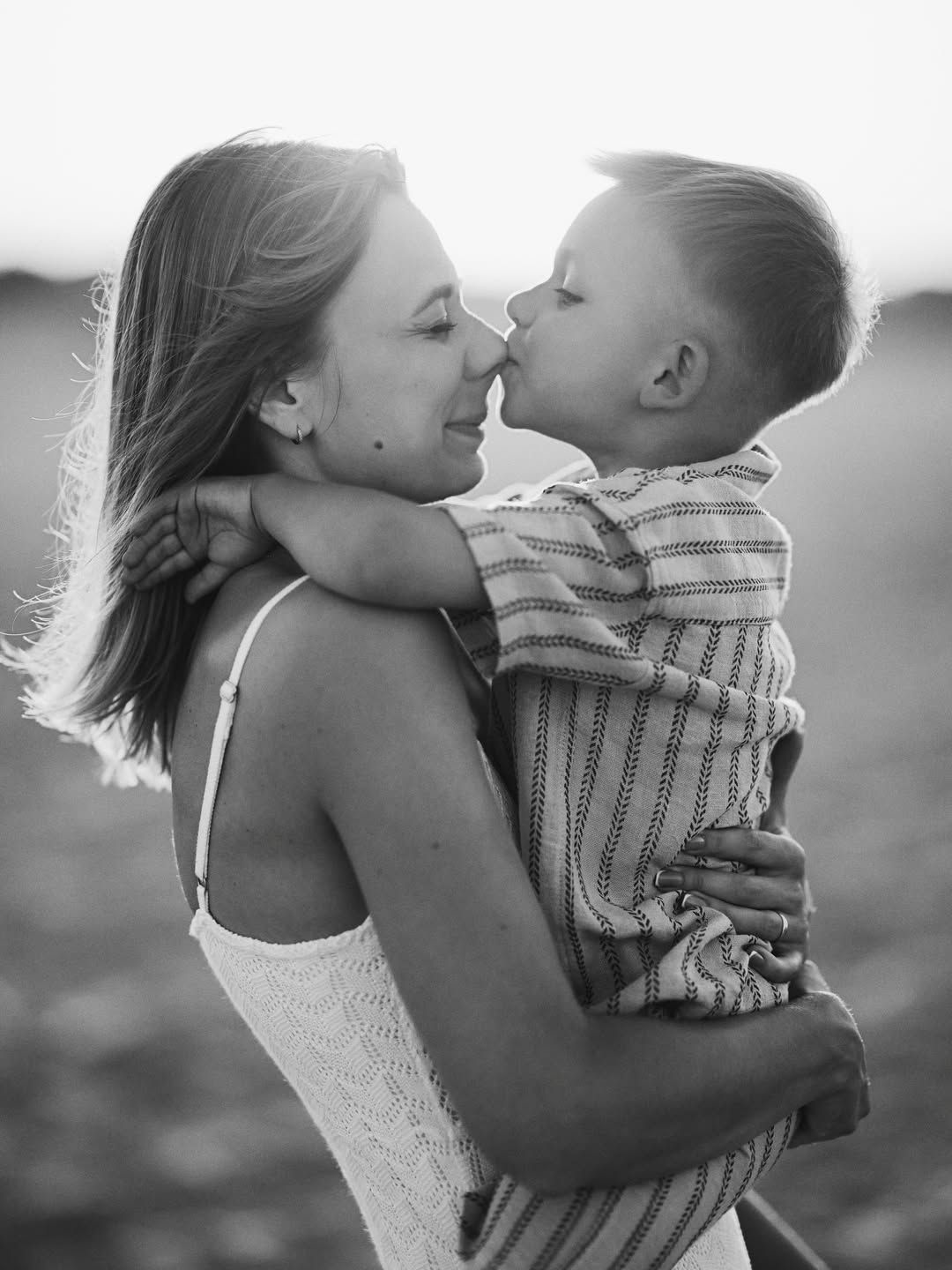 A sweet black and white moment of a little boy kissing his mother on the nose during a beach session in Spain.