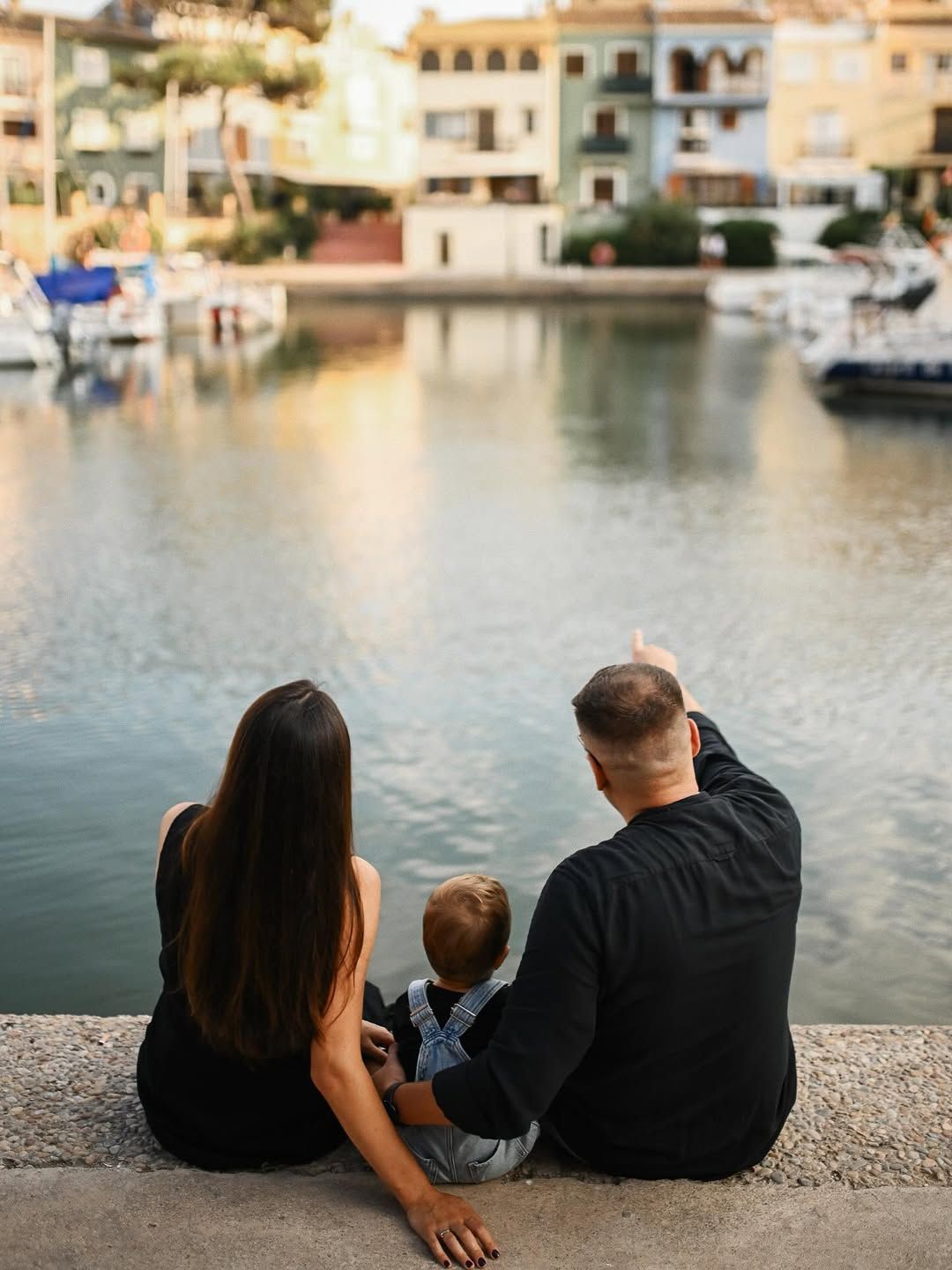 A father points out a view to his wife and son against the vibrant and colorful architectural facades of Port Saplaya.