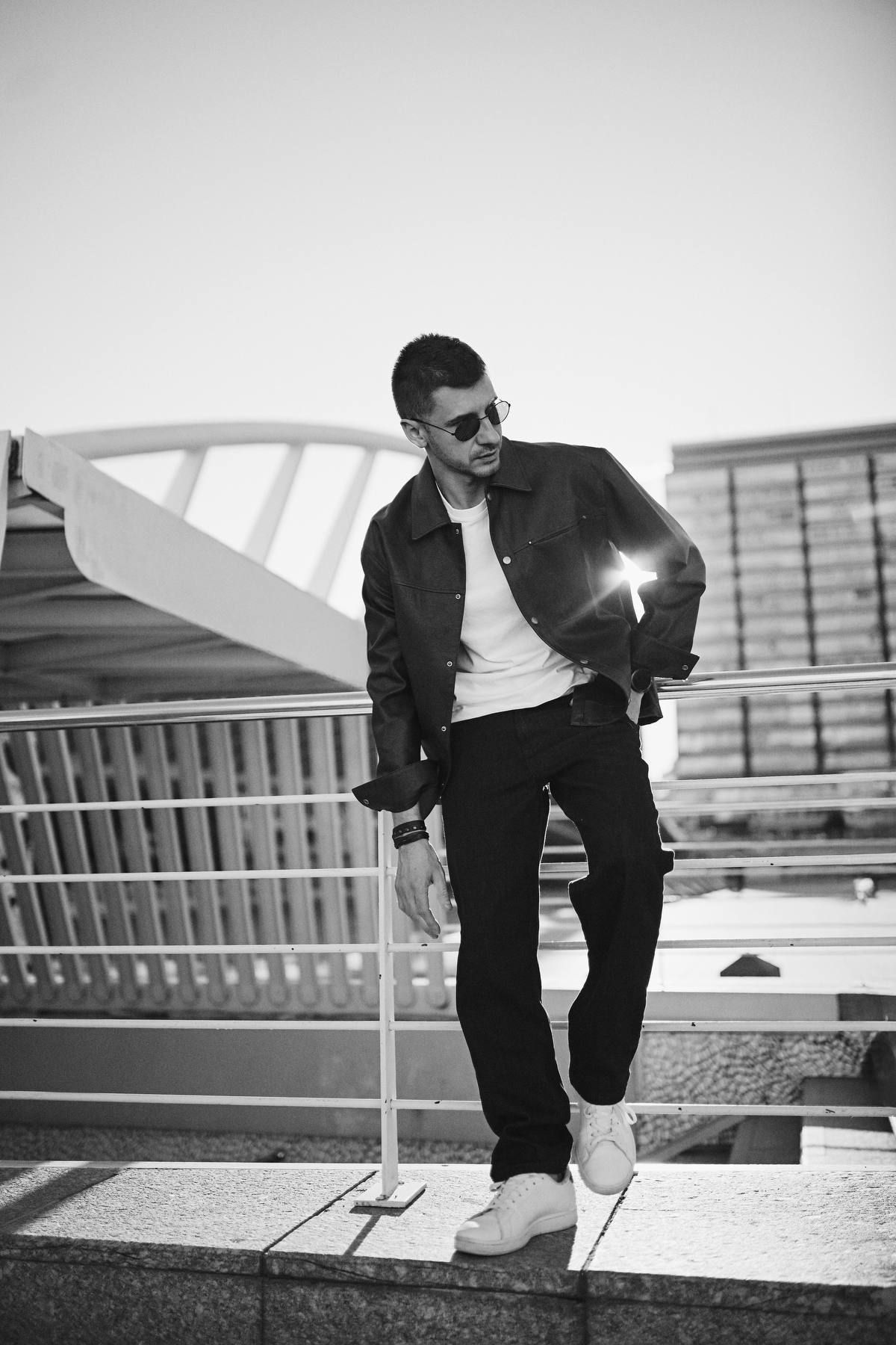 A man in a black leather jacket posing against the clean white minimalist architecture of modern Valencia buildings.
