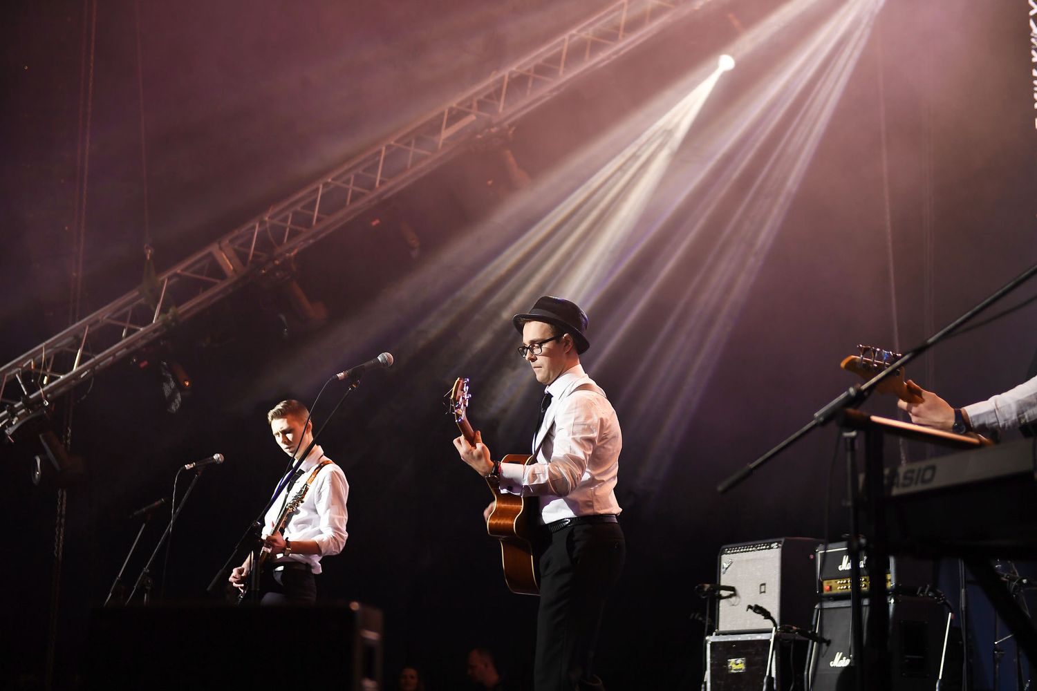 Live cover band with guitarists performing on stage under warm spotlights at a corporate event.