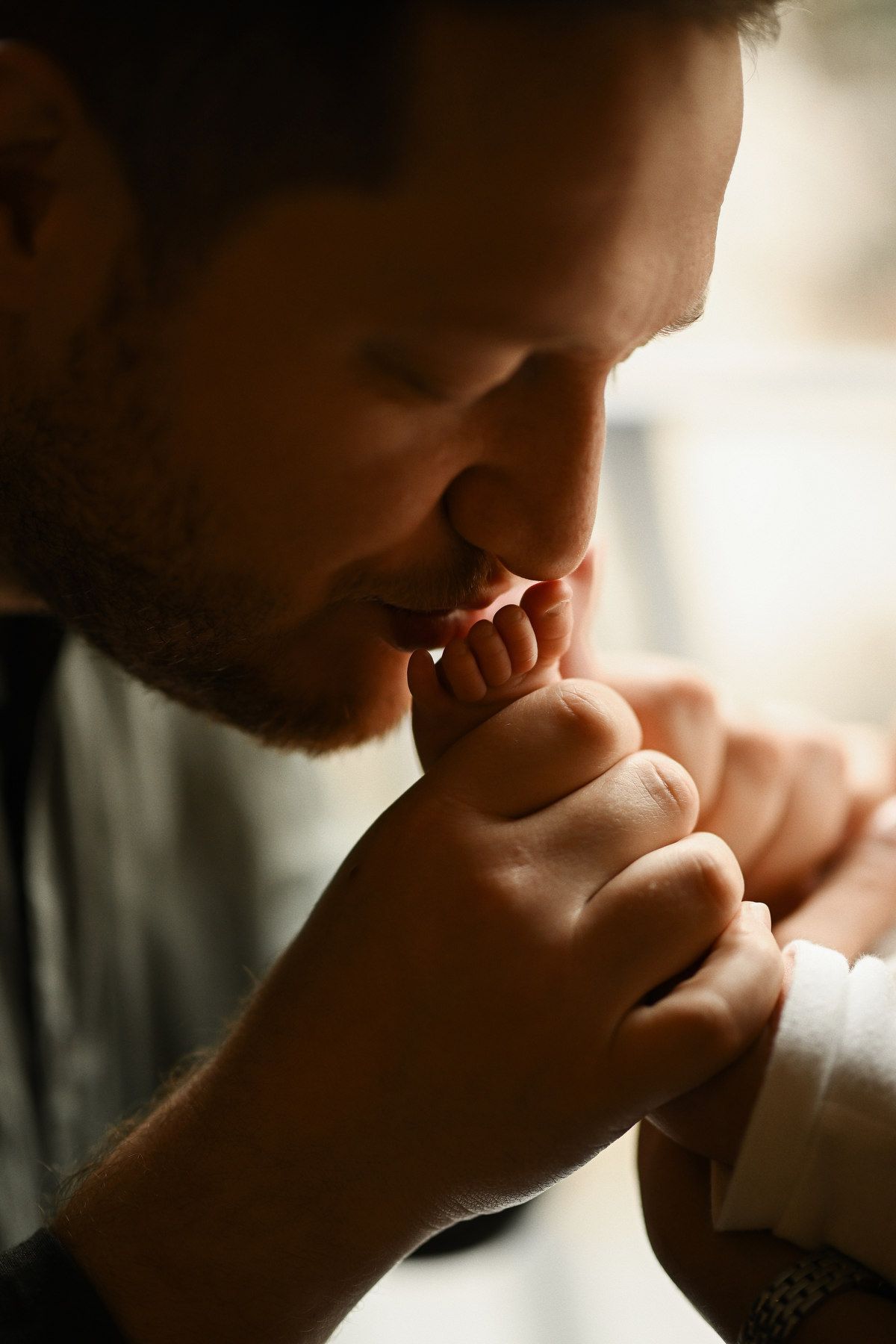 A father tenderly kissing his newborn baby's feet during an emotional lifestyle session at home.