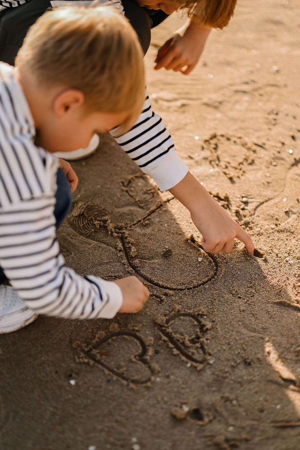Close-up of two young brothers drawing hearts in the wet sand during a playful family photoshoot on a sunny beach in Calpe