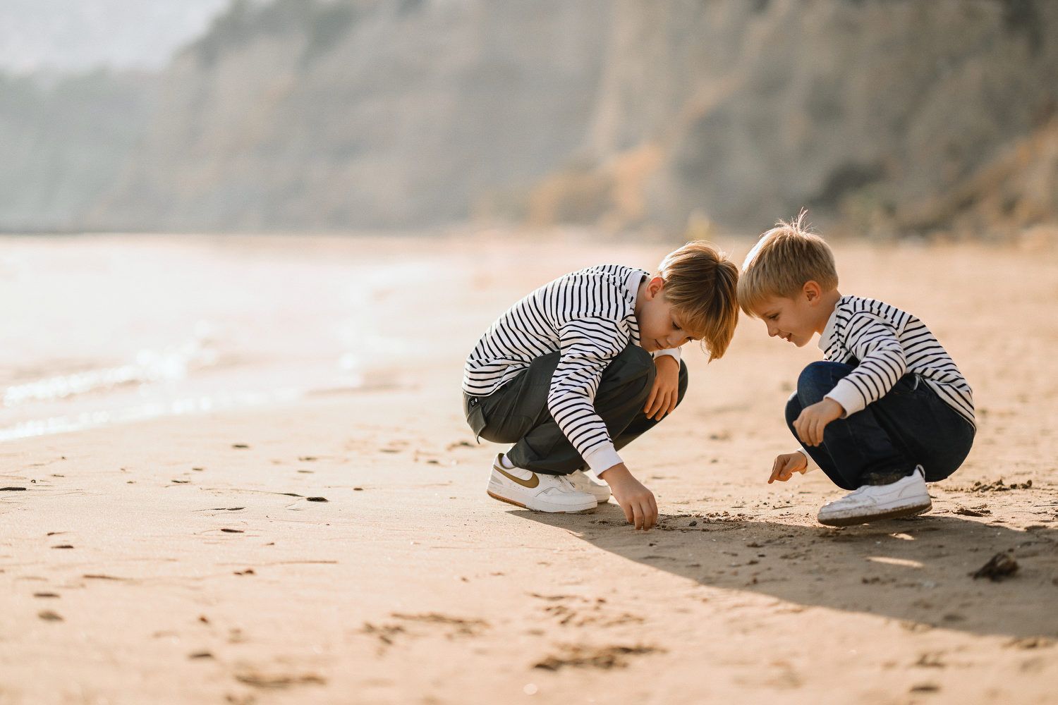 Two young brothers crouching on the beach and drawing in the sand during a candid family photography session in Calpe