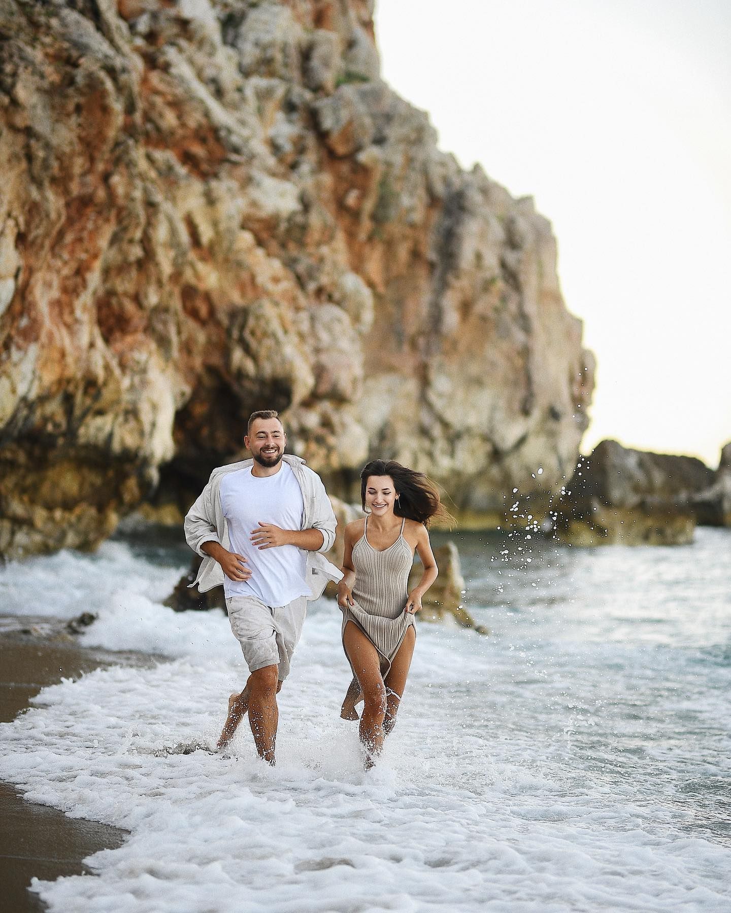 A happy couple running barefoot through the splashing waves on a sandy beach, capturing cinematic memories of their Valencia honeymoon.