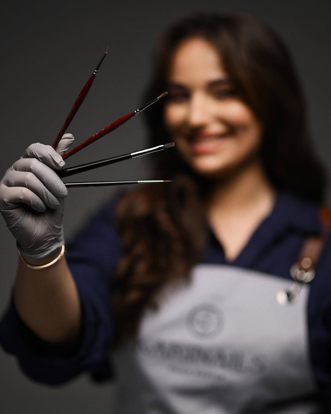 A professional nail artist in an apron holding precision brushes, highlighting the craftsmanship behind her creative business.