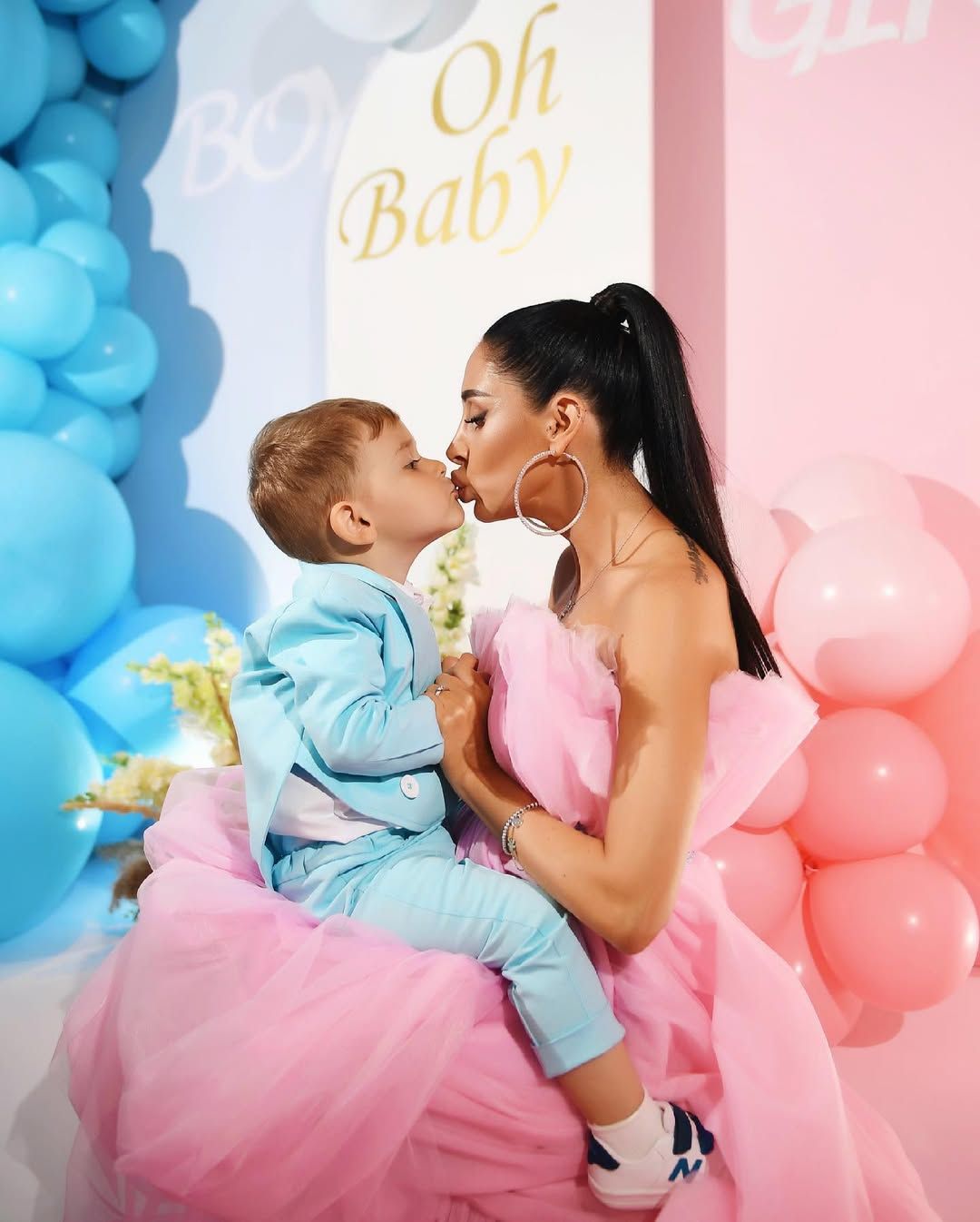 Pregnant mother in a pink gown kissing her son during an elegant indoor baby shower and gender reveal celebration in Valencia.