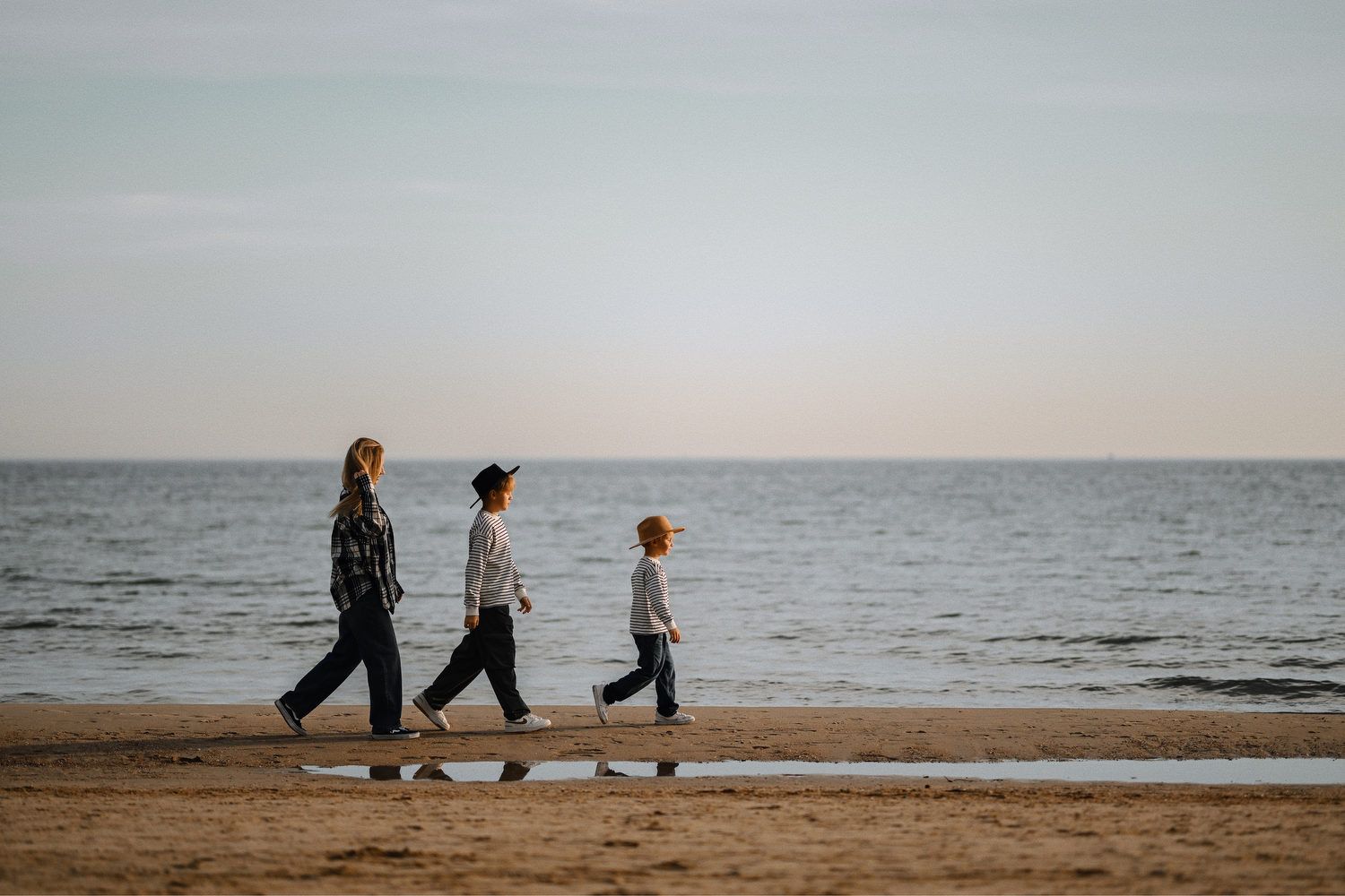 A mother and her children walking along the sandy shoreline with the calm Mediterranean Sea behind them in Calpe