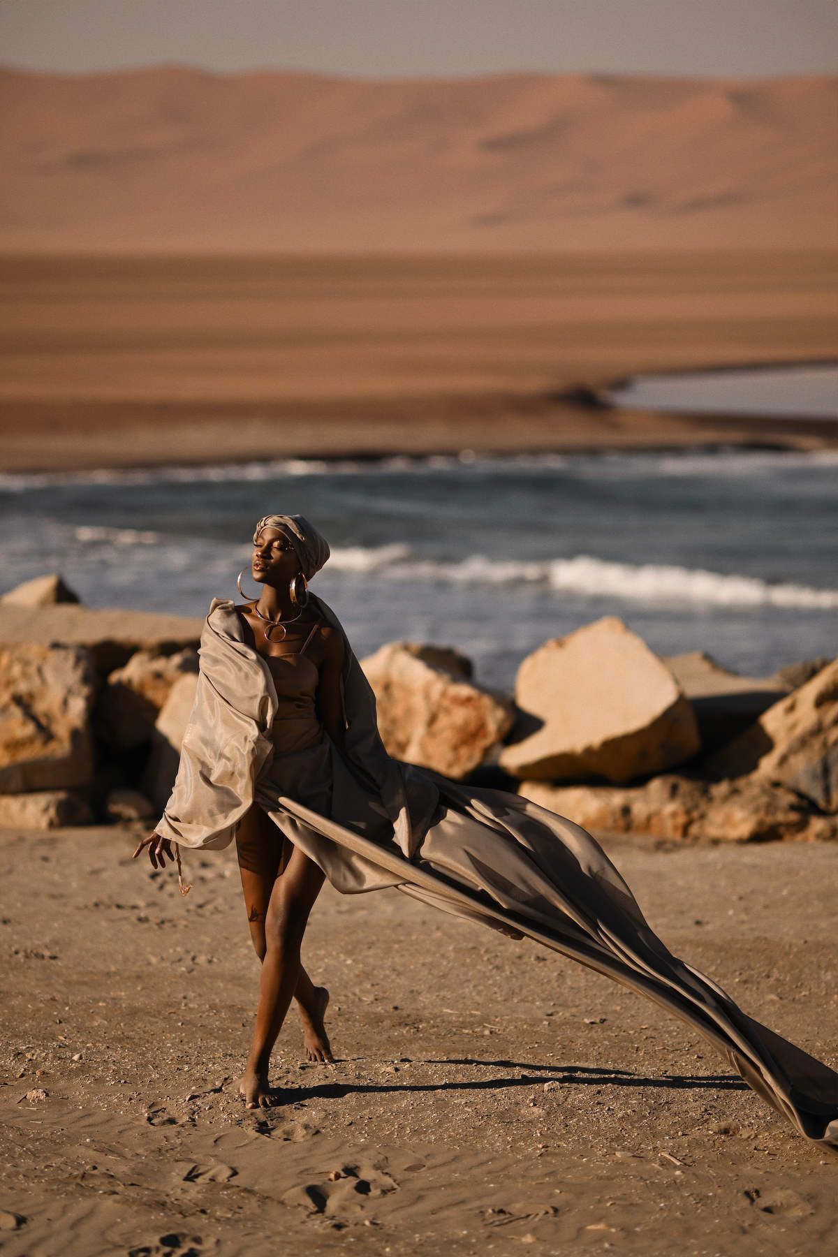 A model posing elegantly in flowing silk resort wear near the coast for an editorial commercial photoshoot.