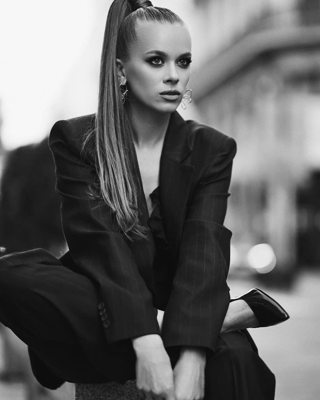 A striking monochrome editorial portrait of a model sitting and looking directly into the camera, capturing an intense fashion mood.