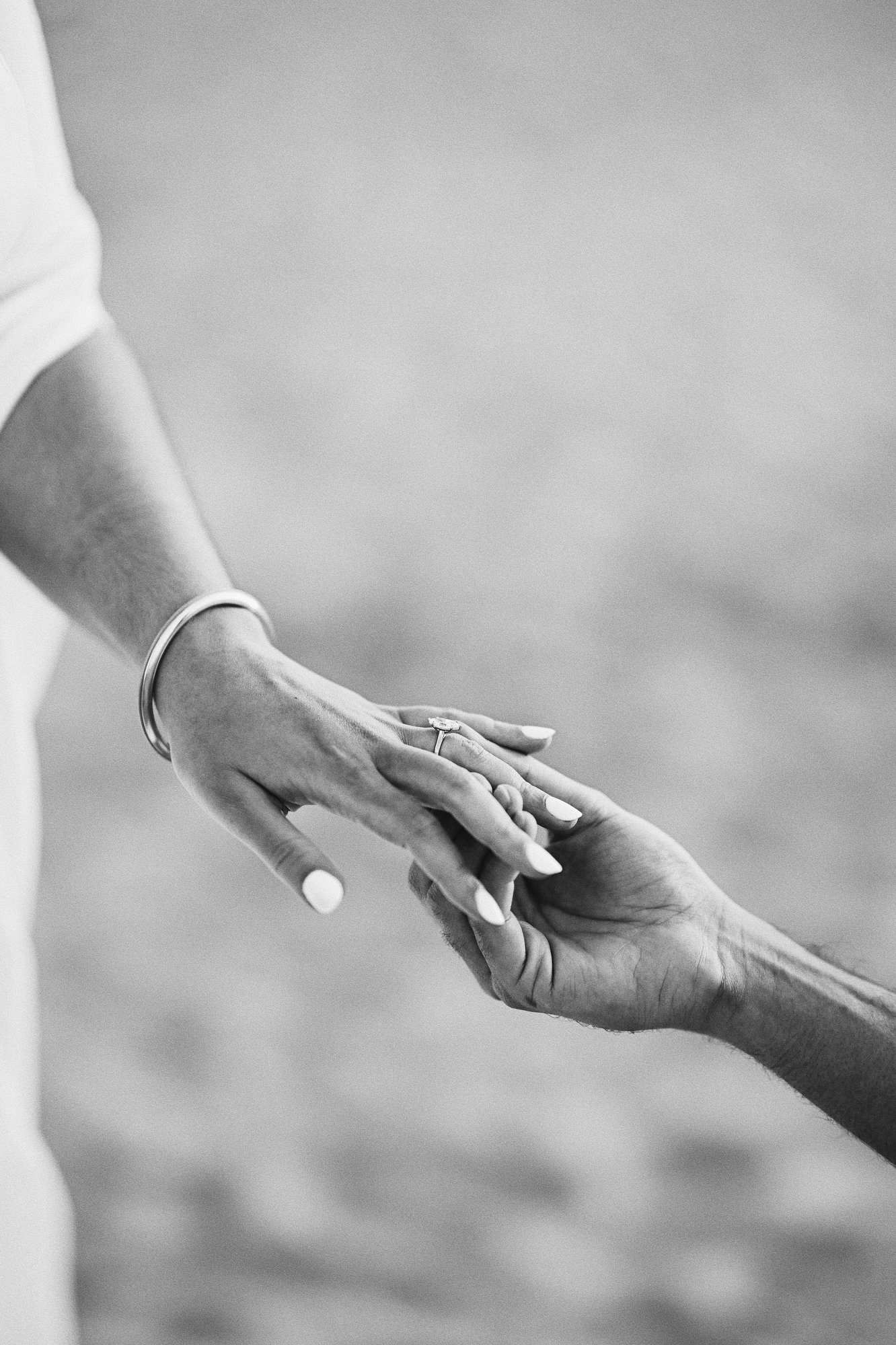A detailed black and white close-up shot showing a man placing a beautiful diamond engagement ring on his partner's finger.