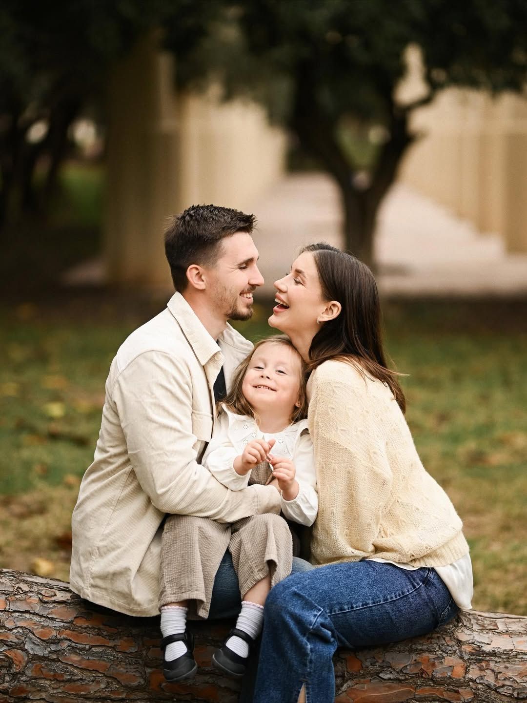 Joyful family gathered on a fallen tree during a maternity session in Turia Park, Valencia with warm natural tones and relaxed expressions.