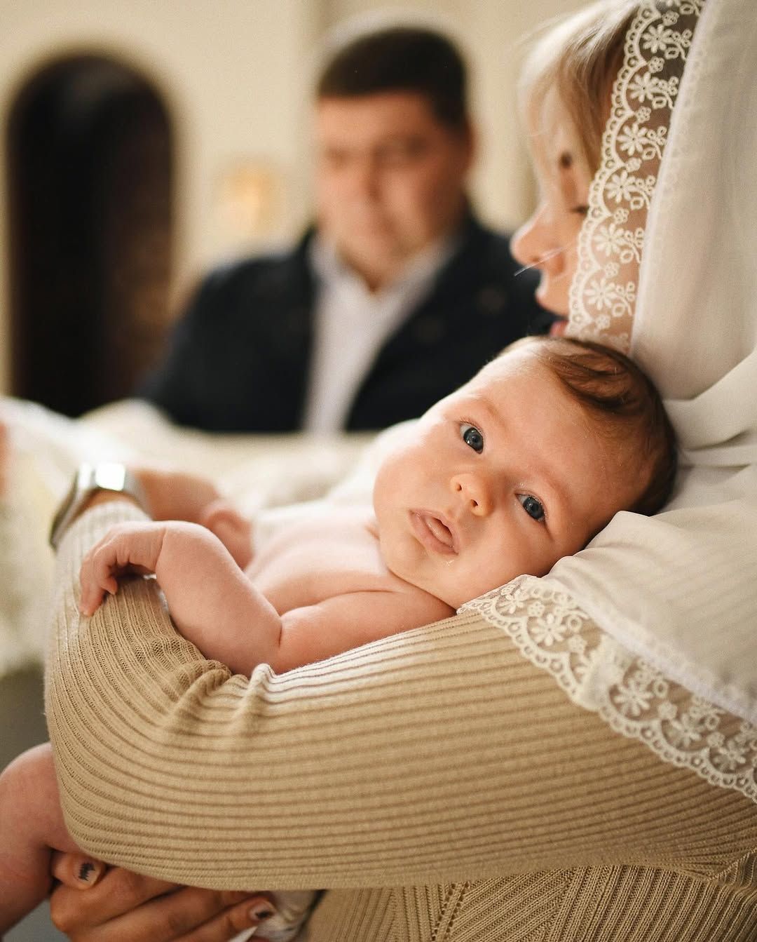 Close-up of a baby held by a godmother wearing a lace head covering inside a Valencia church during a baptism