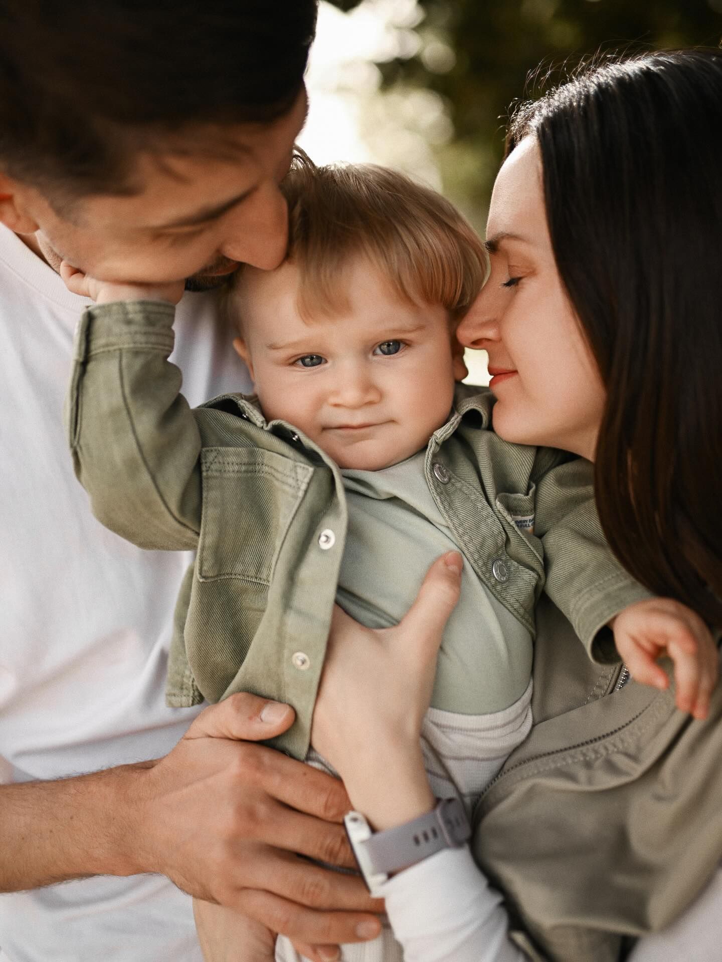Tender close-up of parents embracing their baby boy in a green jacket during a professional family photoshoot in Valencia.